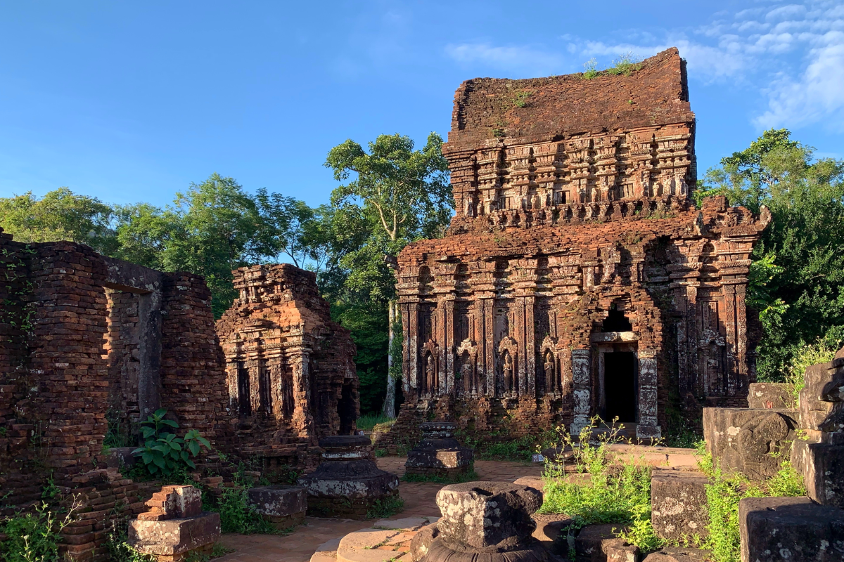 Red brick Hindu temple ruins at My Son Sanctuary surrounded by jungle-covered mountains.